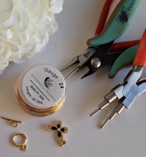 A pair of gold plated earrings alongside pliers and a flower, showcasing a jewelry-making scene.