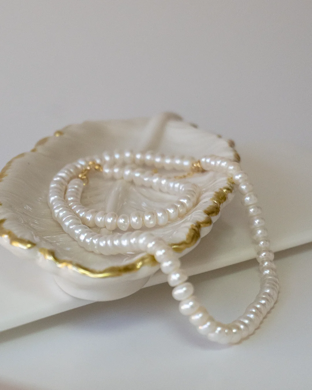 A white pearl necklace elegantly displayed on a gold plate, showcasing its luster and fine craftsmanship.