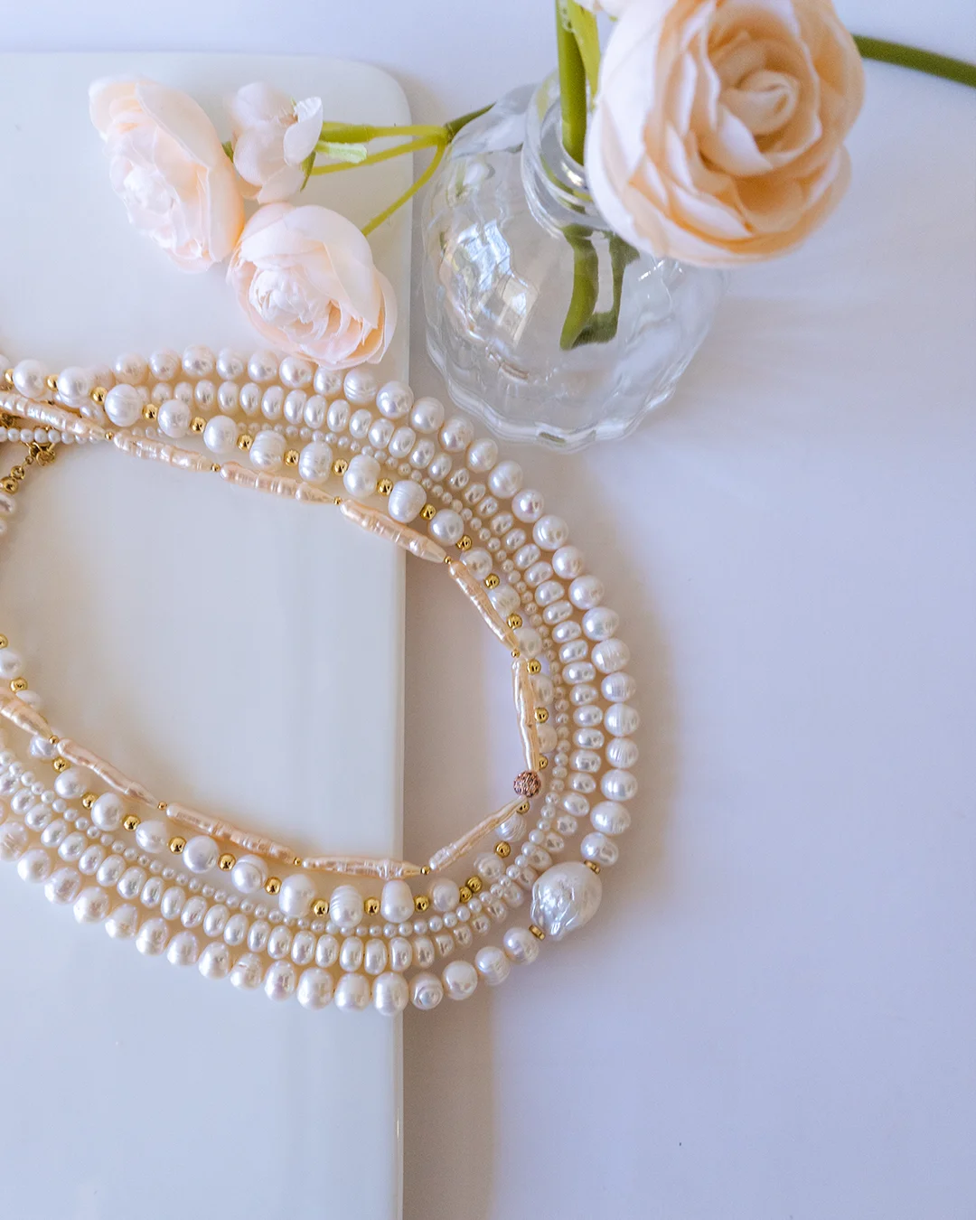 A delicate necklace adorned with pearls and floral accents displayed on a white table.