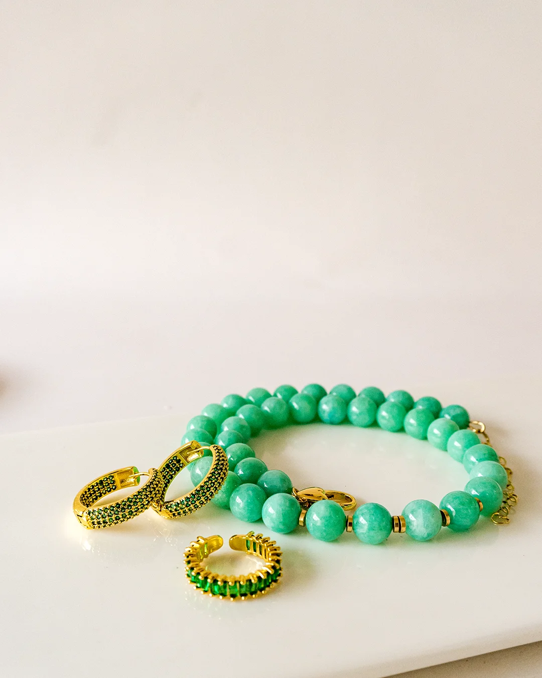 A green bracelet, gold ring, and earrings displayed on a white table surface.